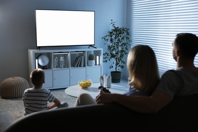 Happy family with snacks and drinks watching tv together at home, back view