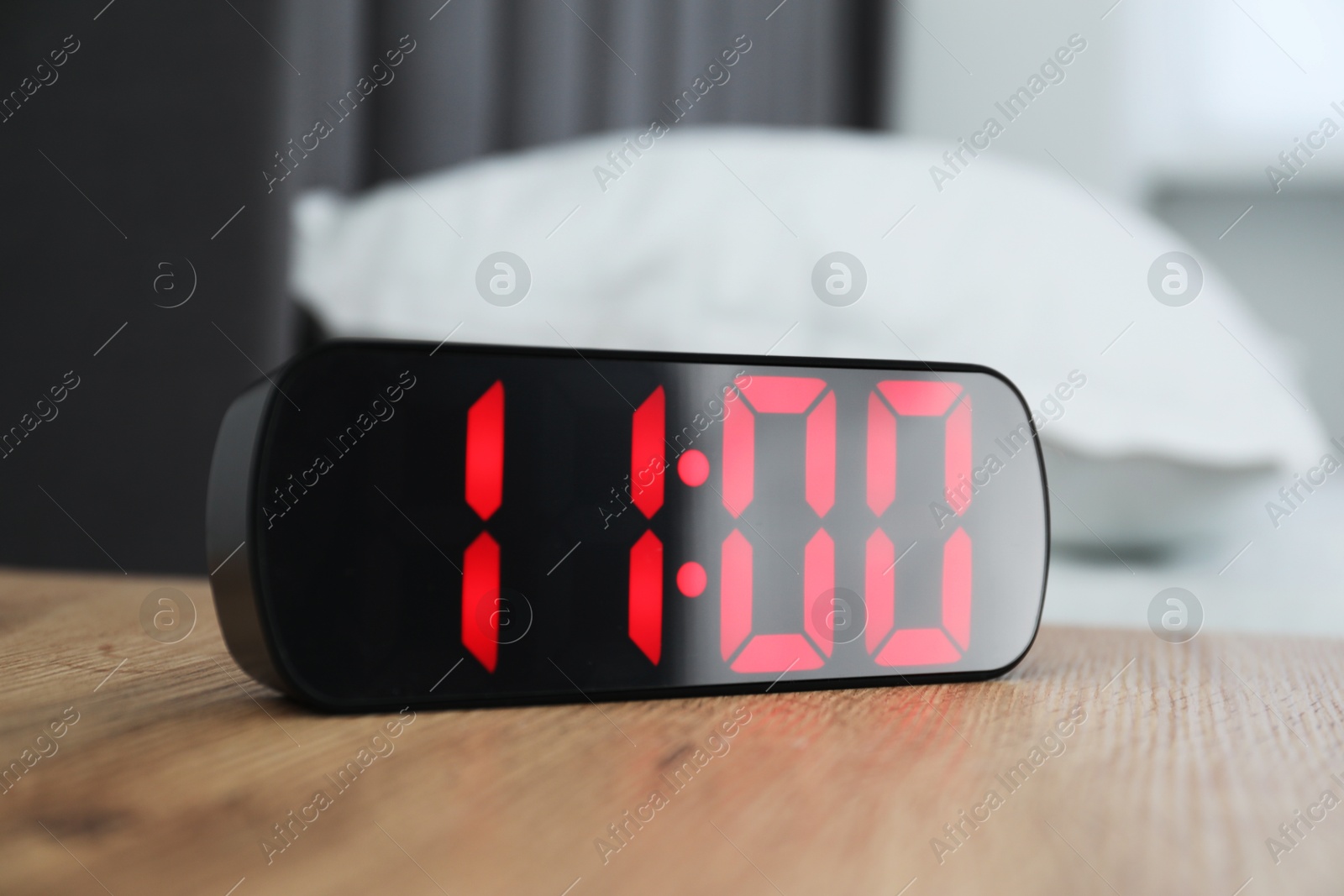 Photo of Digital alarm clock showing 11:00 o'clock on bedside table indoors
