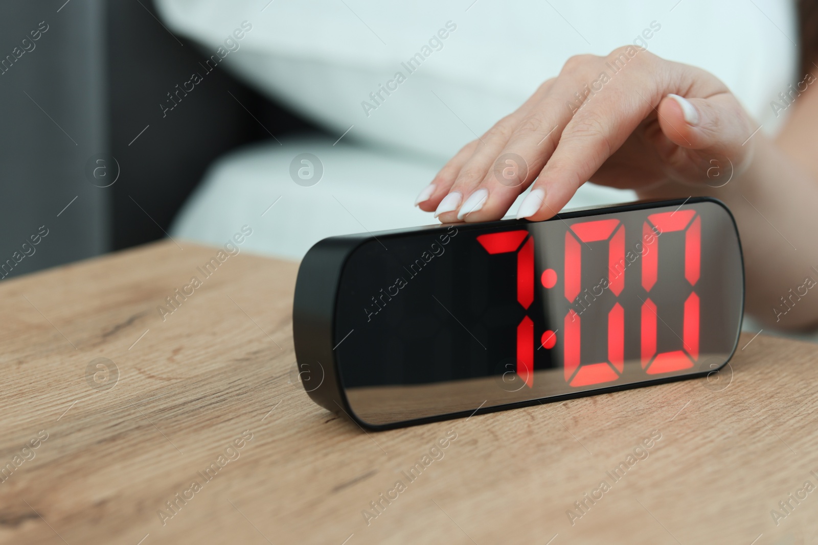 Woman turning off digital alarm clock on bedside table indoors, closeup Photo of Woman turning off digital alarm clock on bedside table indoors, closeup