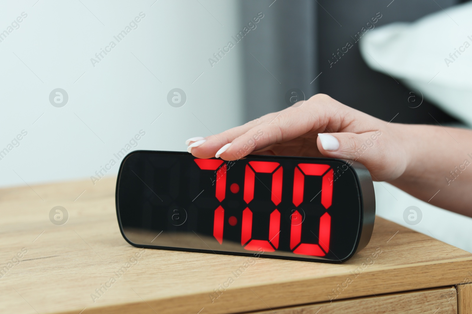 Woman turning off digital alarm clock on bedside table indoors, closeup Photo of Woman turning off digital alarm clock on bedside table indoors, closeup