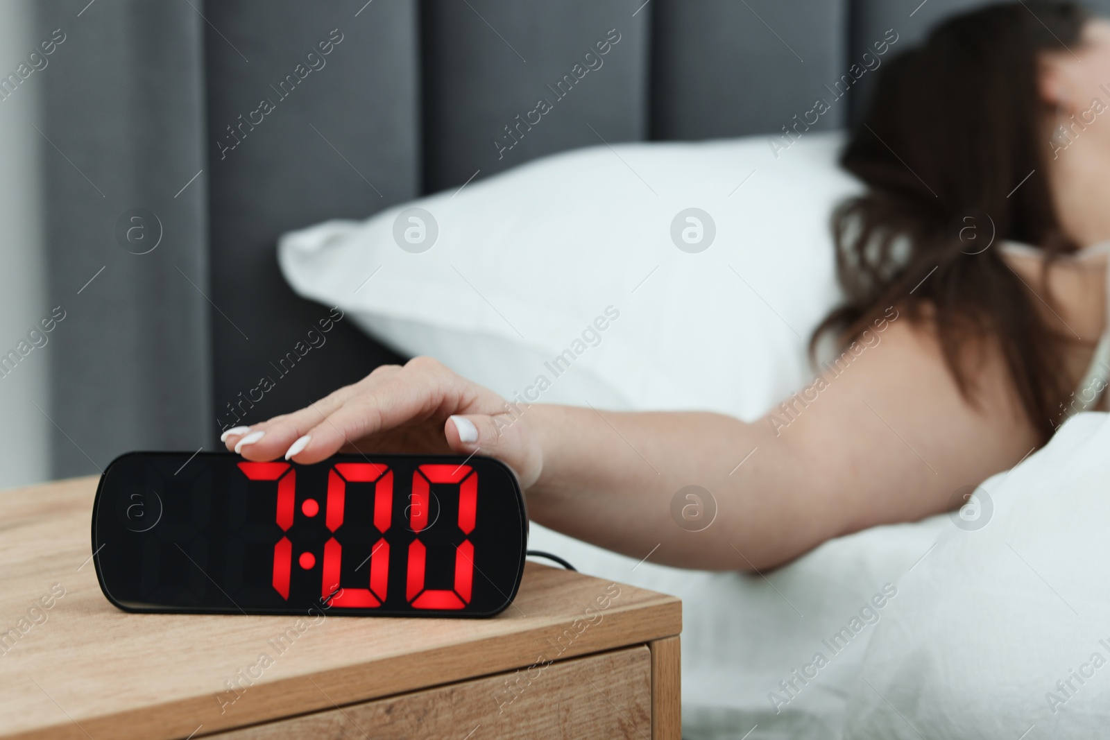 Woman turning off digital alarm clock on bedside table indoors, closeup Photo of Woman turning off digital alarm clock on bedside table indoors, closeup