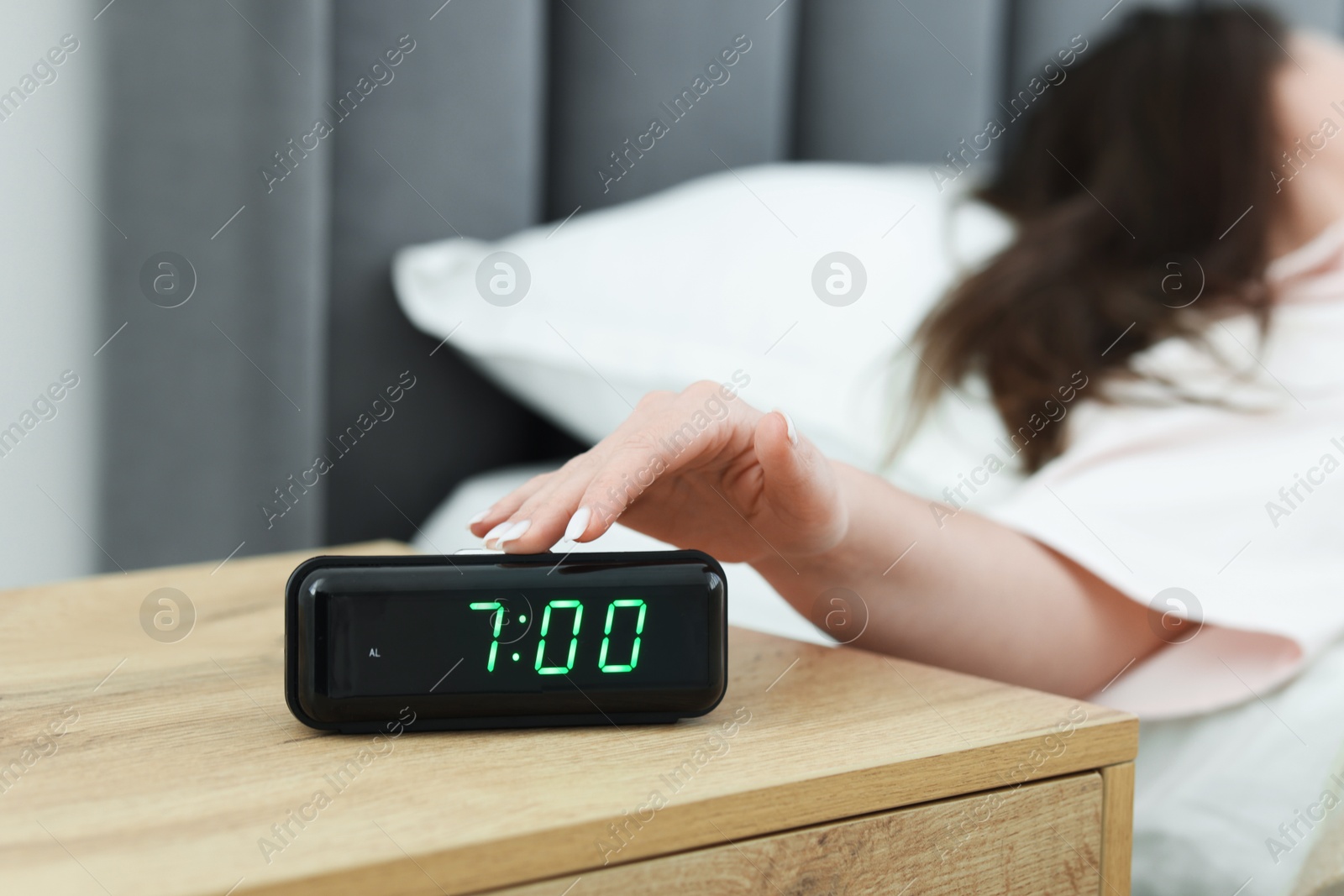 Woman turning off digital alarm clock on bedside table indoors, closeup Photo of Woman turning off digital alarm clock on bedside table indoors, closeup