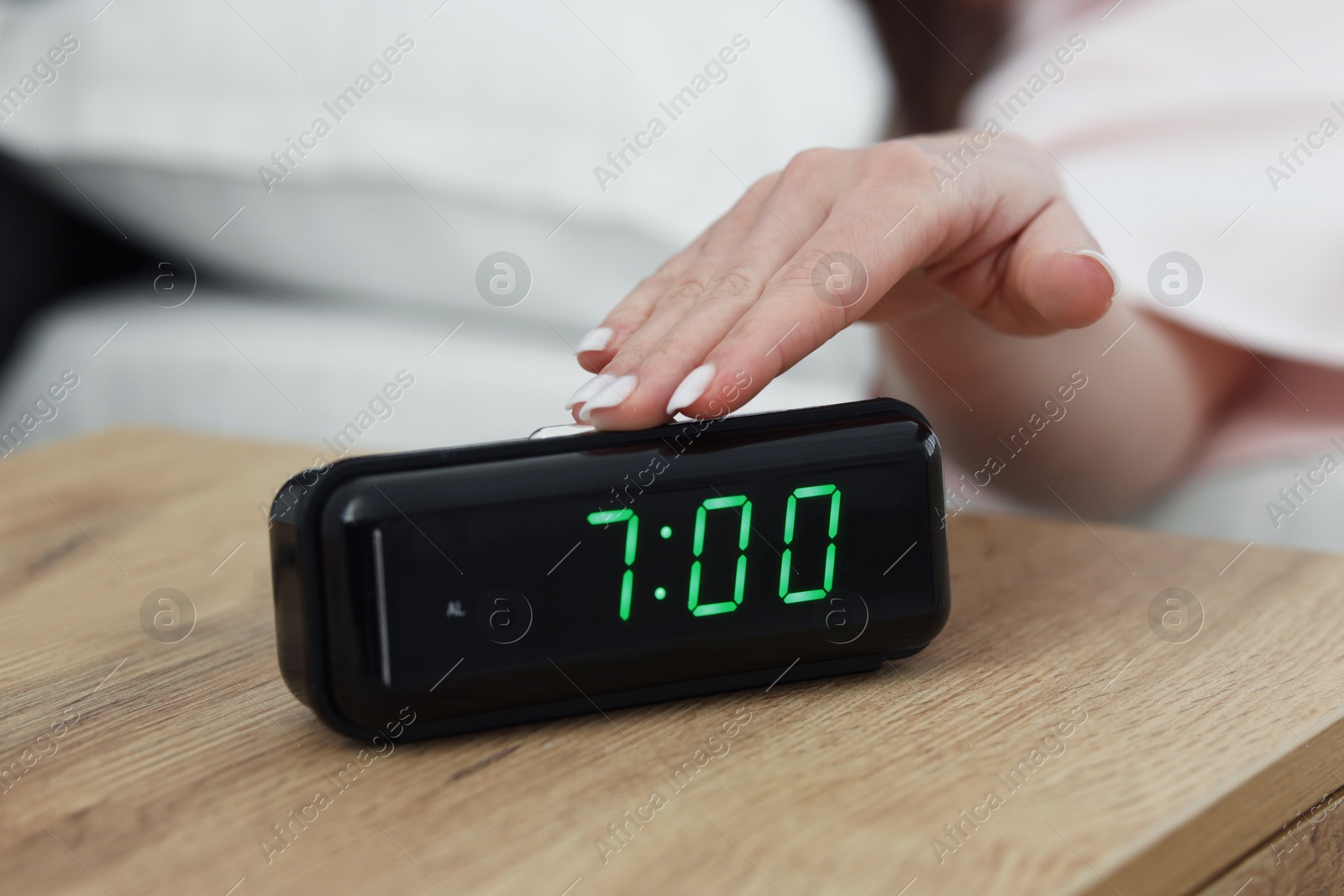 Woman turning off digital alarm clock on bedside table indoors, closeup Photo of Woman turning off digital alarm clock on bedside table indoors, closeup