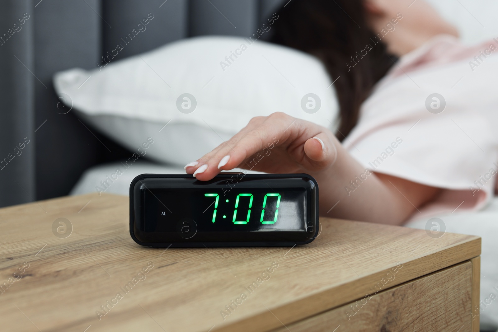 Woman turning off digital alarm clock on bedside table indoors, closeup Photo of Woman turning off digital alarm clock on bedside table indoors, closeup