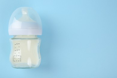 Feeding bottle with milk on light blue background, top view. Space for text