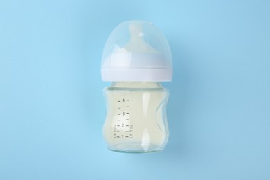 Feeding bottle with milk on light blue background, top view