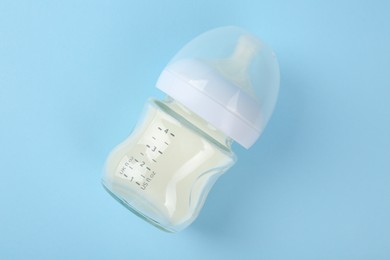 Photo of Feeding bottle with milk on light blue background, top view