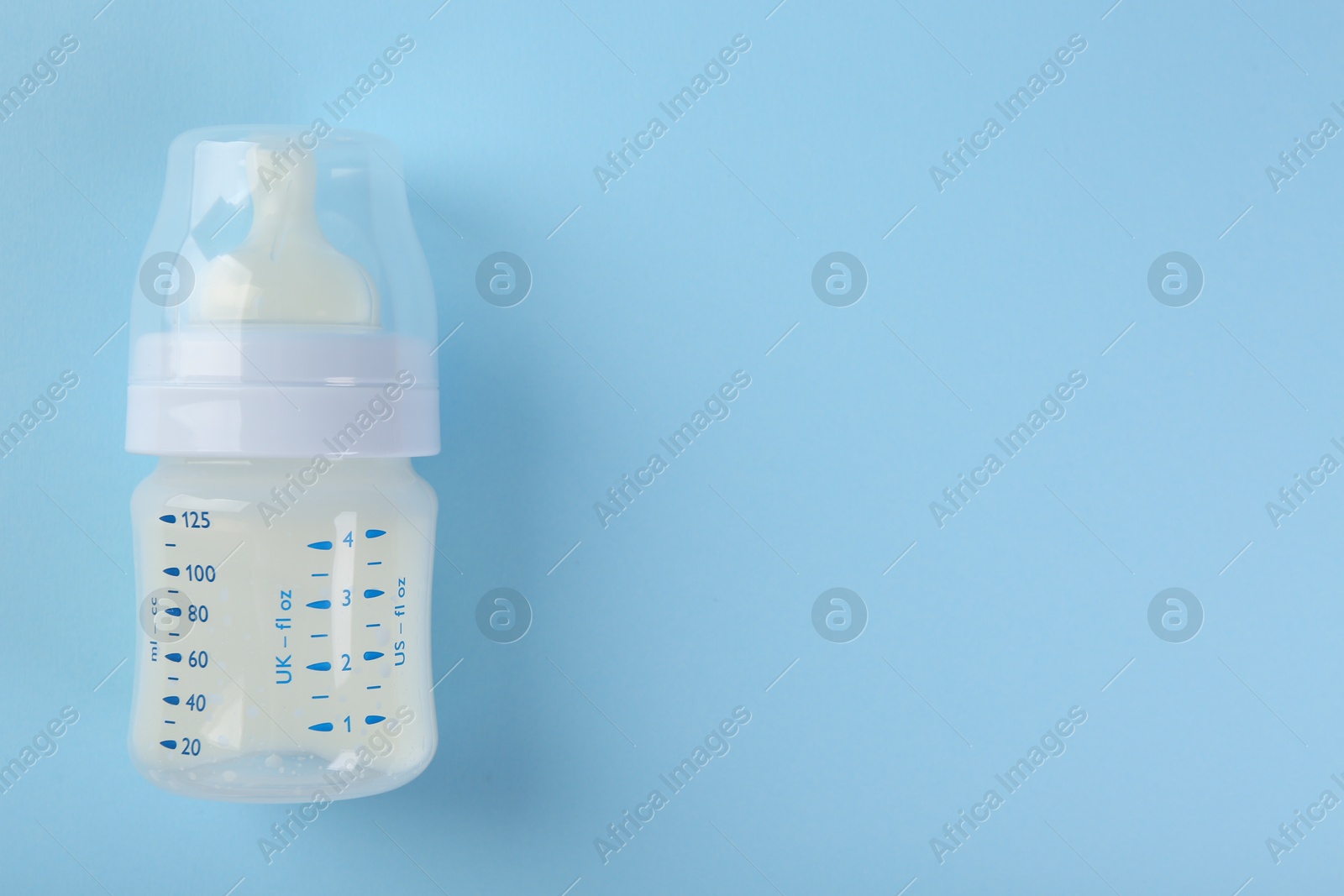 Photo of Feeding bottle with milk on light blue background, top view. Space for text