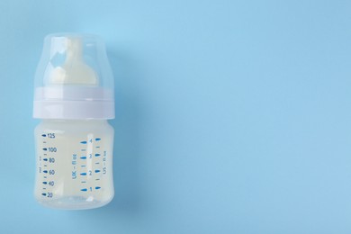 Photo of Feeding bottle with milk on light blue background, top view. Space for text