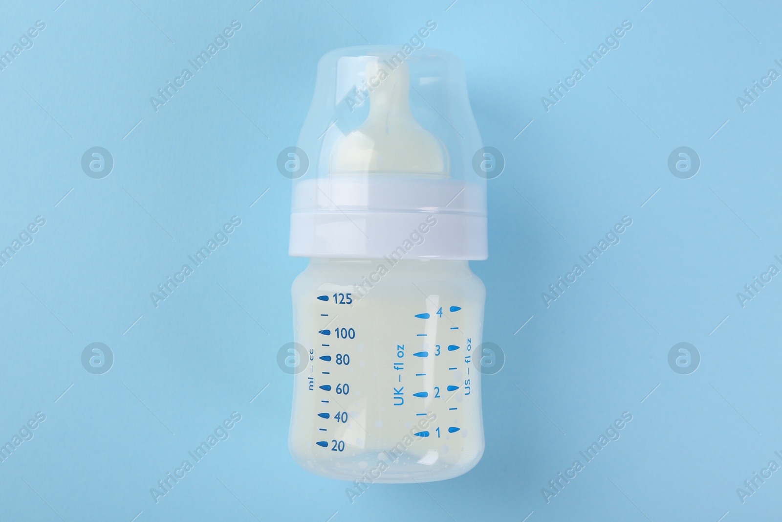 Photo of Feeding bottle with milk on light blue background, top view