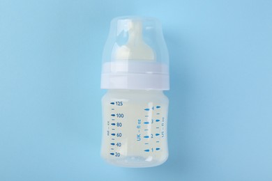 Feeding bottle with milk on light blue background, top view