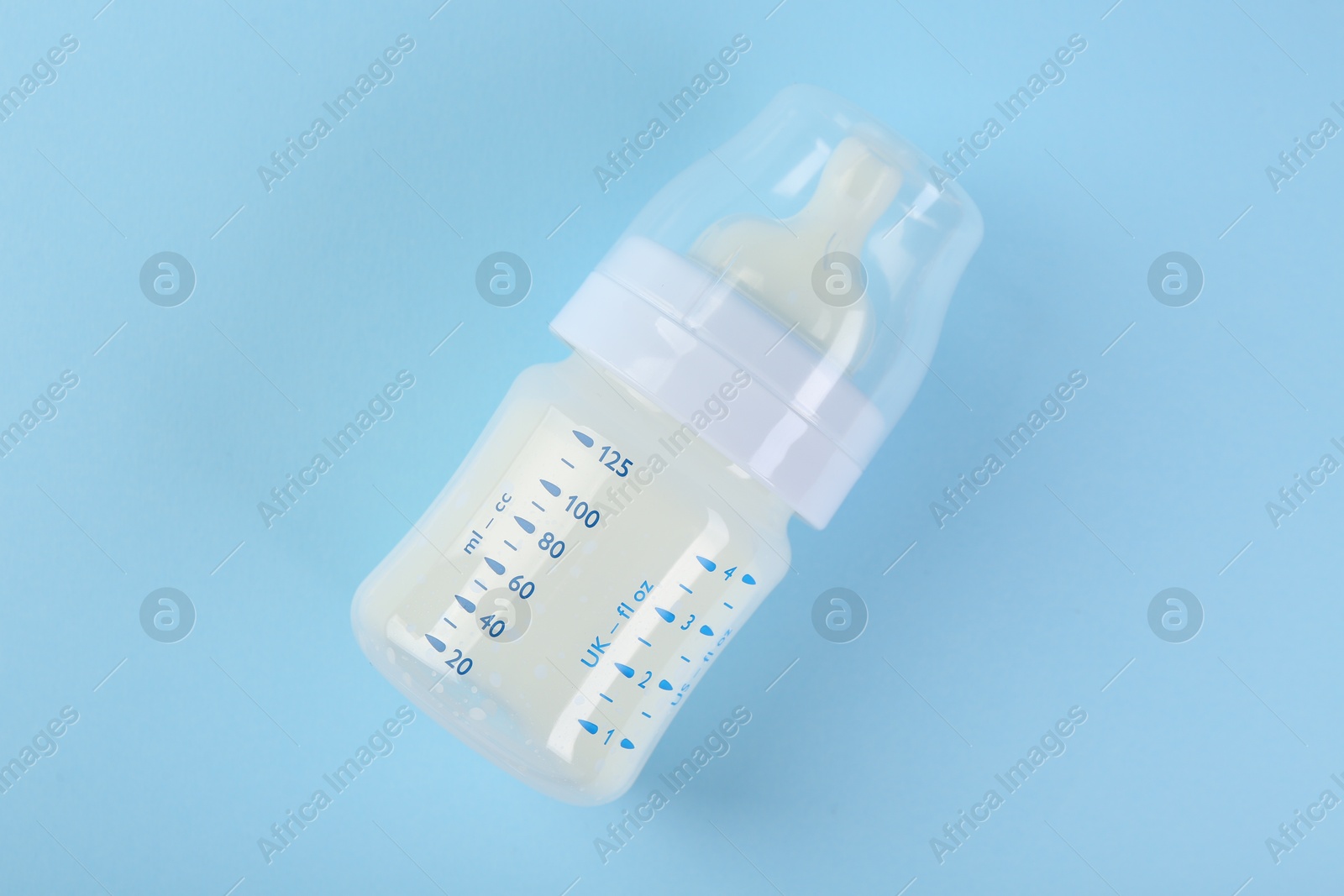 Photo of Feeding bottle with milk on light blue background, top view