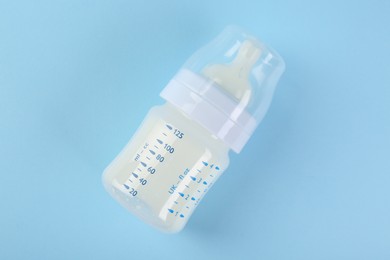 Feeding bottle with milk on light blue background, top view