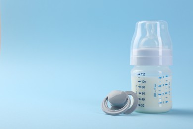 Feeding bottle with milk and pacifier on light blue background, space for text