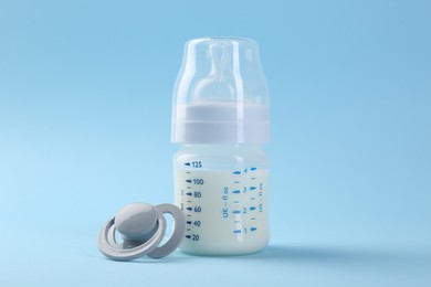 Photo of Feeding bottle with milk and pacifier on light blue background