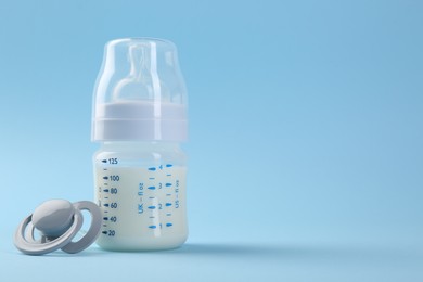 Feeding bottle with milk and pacifier on light blue background, space for text