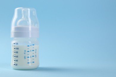 Photo of Feeding bottle with milk on light blue background, space for text