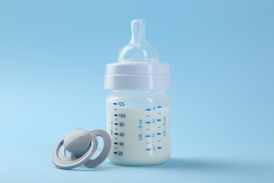 Feeding bottle with milk and pacifier on light blue background