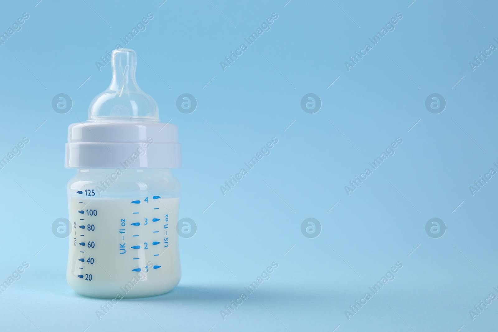 Photo of Feeding bottle with milk on light blue background, space for text