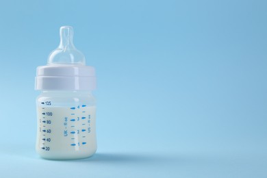 Feeding bottle with milk on light blue background, space for text