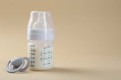 Feeding bottle with milk and pacifier on beige background, space for text