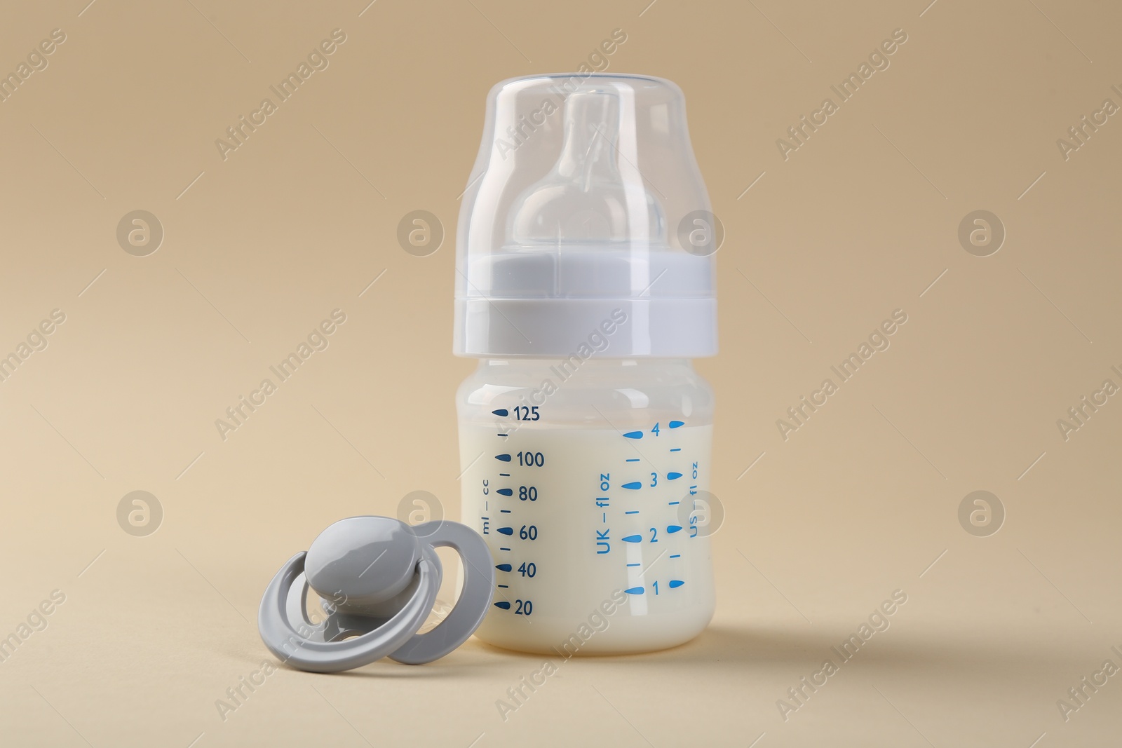 Photo of Feeding bottle with milk and pacifier on beige background