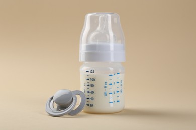 Photo of Feeding bottle with milk and pacifier on beige background