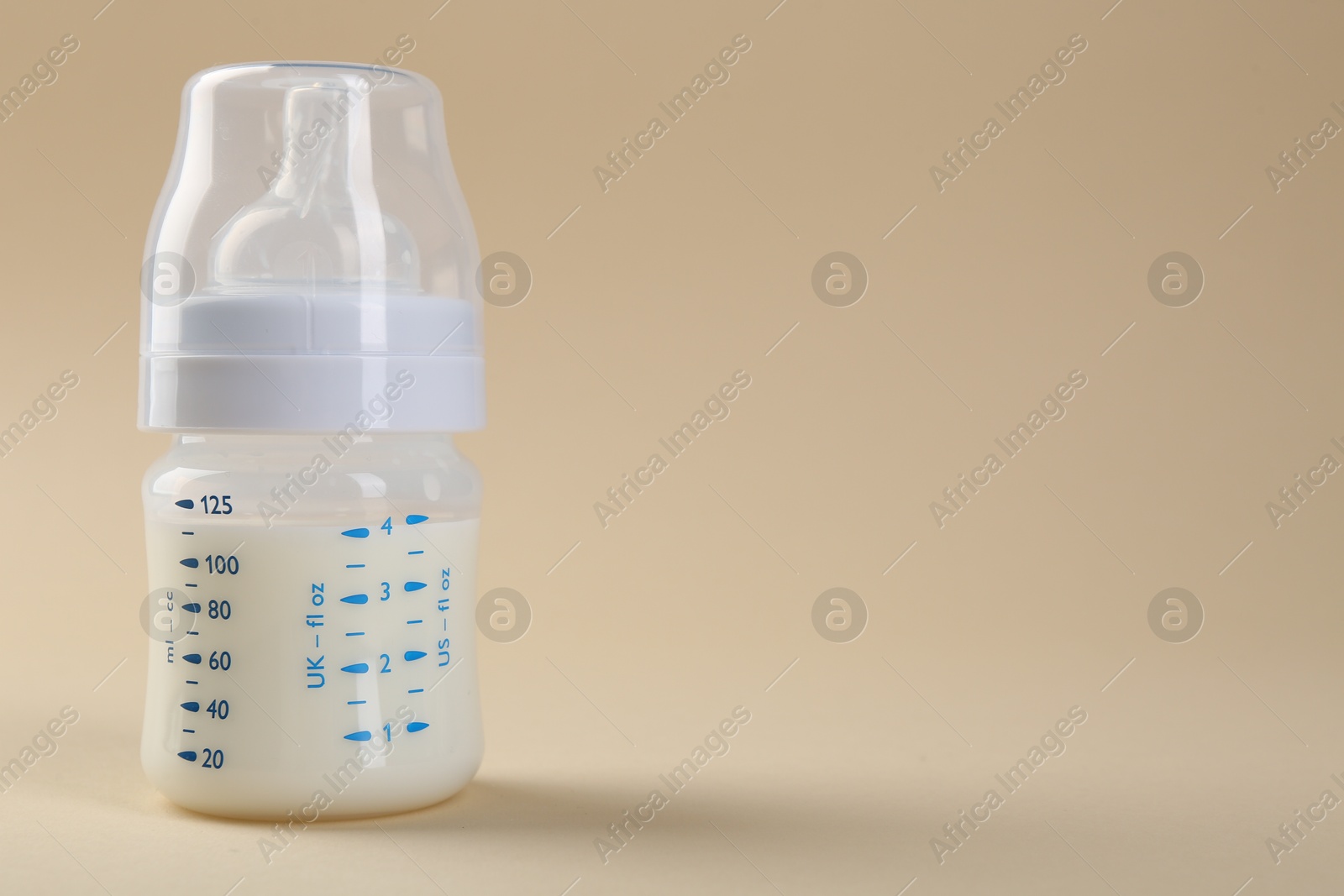 Photo of Feeding bottle with milk on beige background, space for text