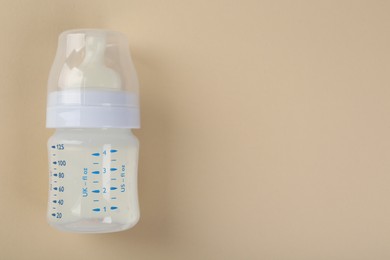 Photo of Feeding bottle with milk on beige background, top view. Space for text