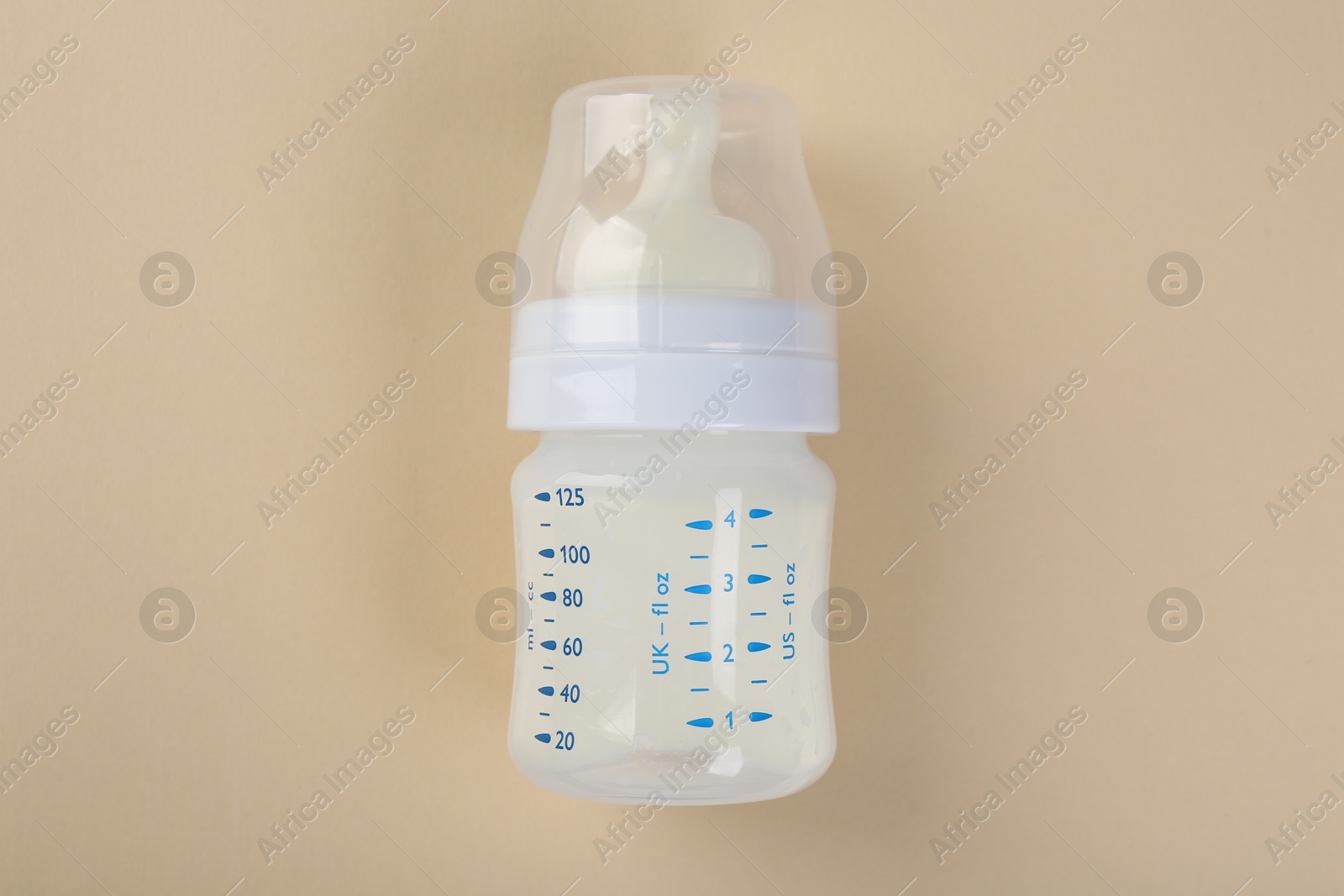 Photo of Feeding bottle with milk on beige background, top view