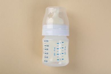 Feeding bottle with milk on beige background, top view