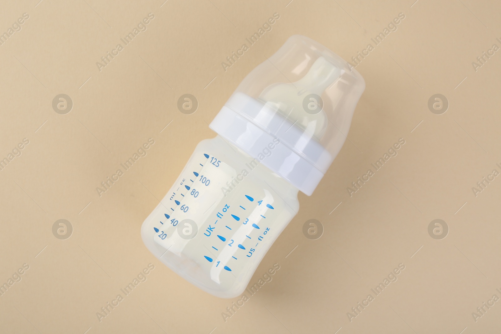 Photo of Feeding bottle with milk on beige background, top view