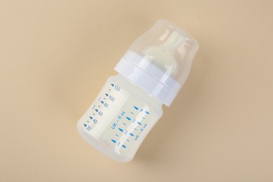 Feeding bottle with milk on beige background, top view