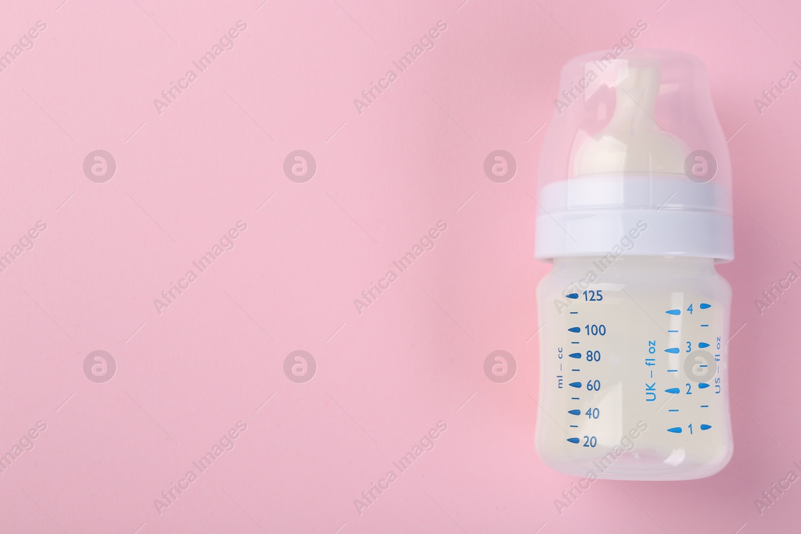 Photo of Feeding bottle with milk on pink background, top view. Space for text