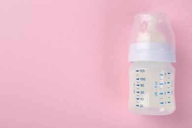 Feeding bottle with milk on pink background, top view. Space for text