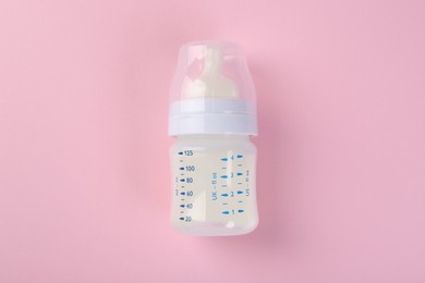 Feeding bottle with milk on pink background, top view