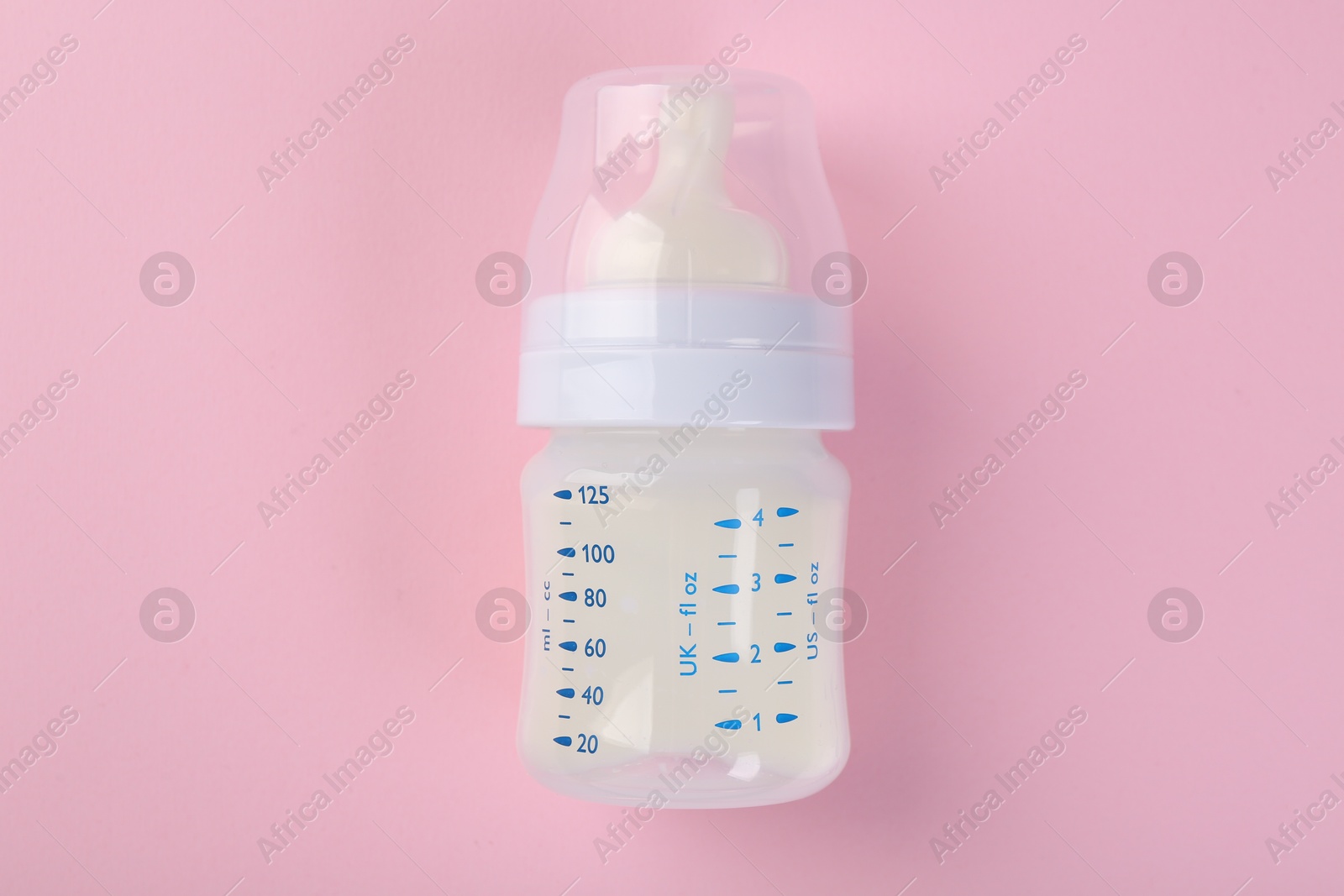 Photo of Feeding bottle with milk on pink background, top view