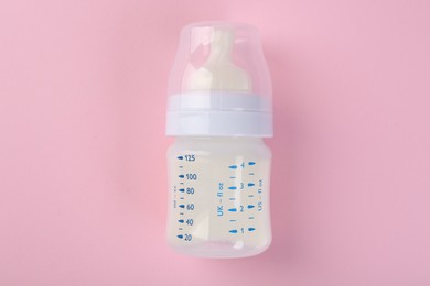 Photo of Feeding bottle with milk on pink background, top view