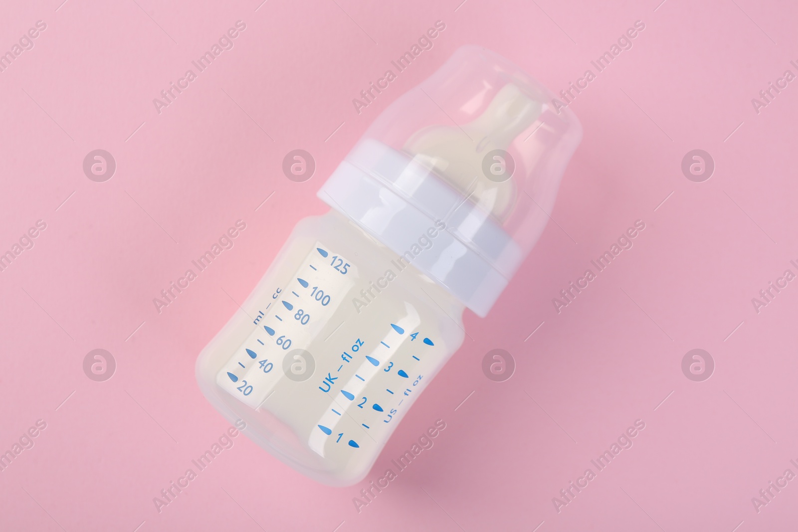 Photo of Feeding bottle with milk on pink background, top view