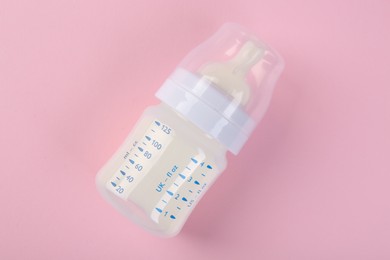 Feeding bottle with milk on pink background, top view