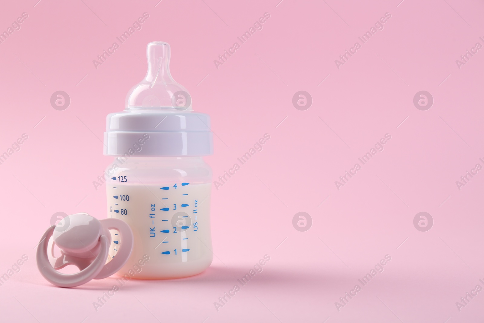 Photo of Feeding bottle with milk and pacifier on pink background, space for text