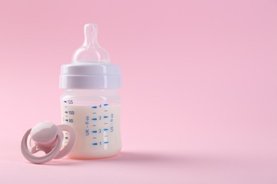 Feeding bottle with milk and pacifier on pink background, space for text