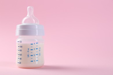 Feeding bottle with milk on pink background, space for text