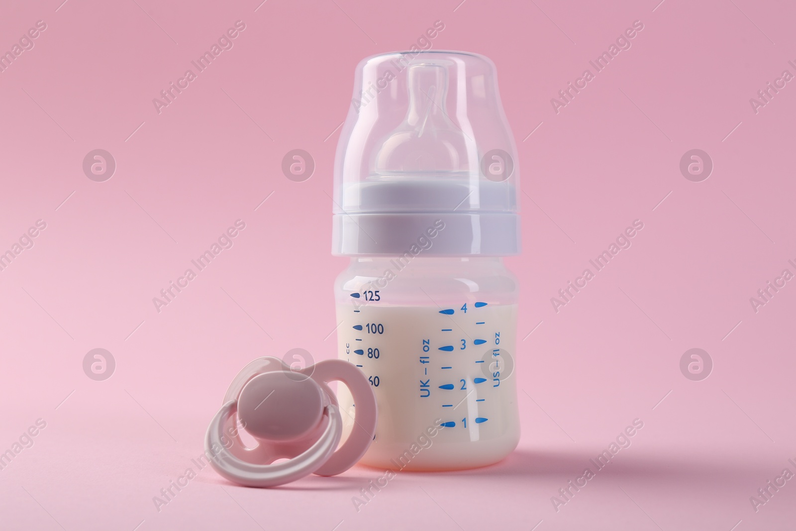 Photo of Feeding bottle with milk and pacifier on pink background