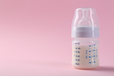 Feeding bottle with milk on pink background, space for text