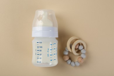 Feeding bottle with milk and teether on beige background, flat lay