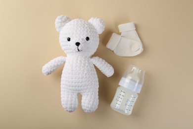 Feeding bottle with milk, baby socks and toy on beige background, flat lay