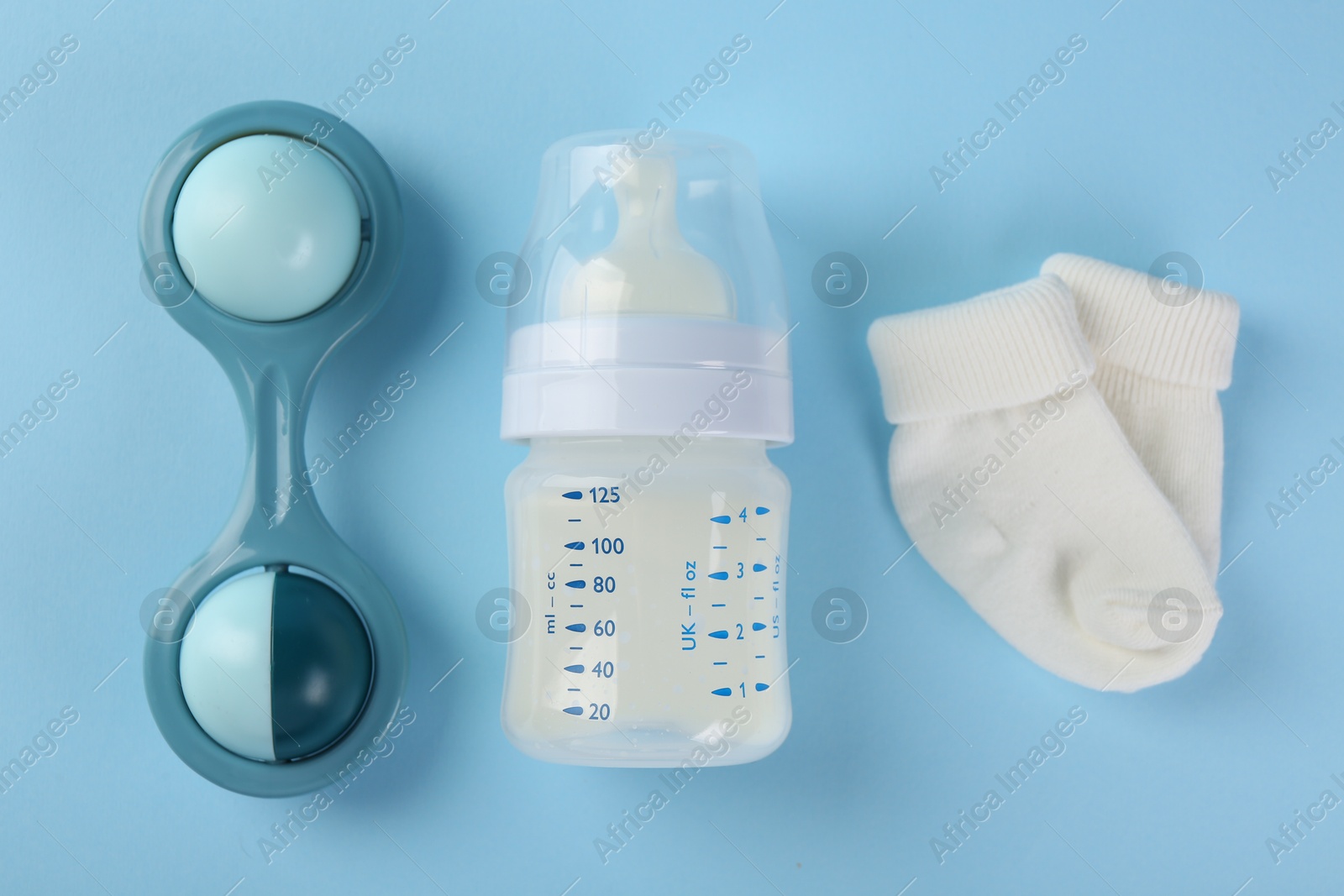 Photo of Feeding bottle with milk, toy and baby socks on light blue background, flat lay