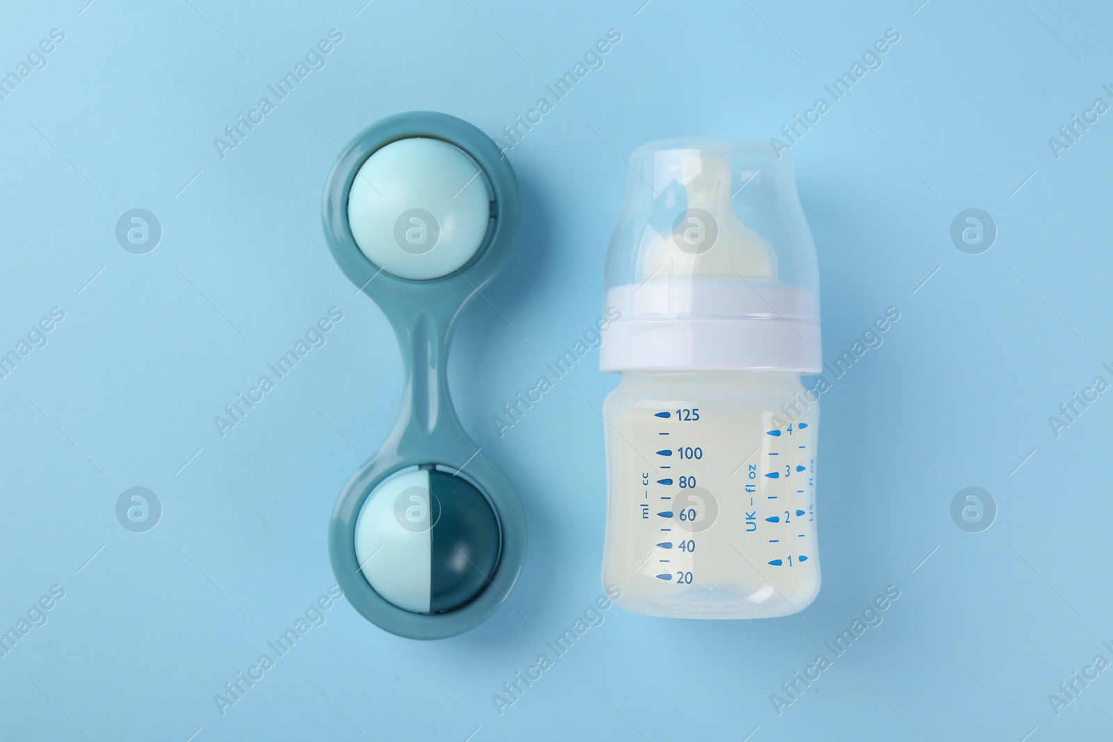 Photo of Feeding bottle with milk and toy on light blue background, flat lay