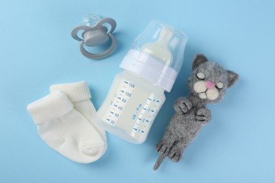 Feeding bottle with milk, toy, baby socks and pacifier on light blue background, flat lay